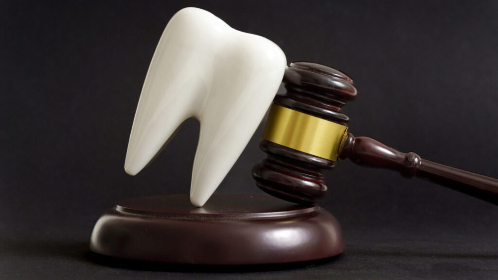 Tooth and judge's gavel symbolizing dental malpractice or legal dispute in dentistry, isolated on black