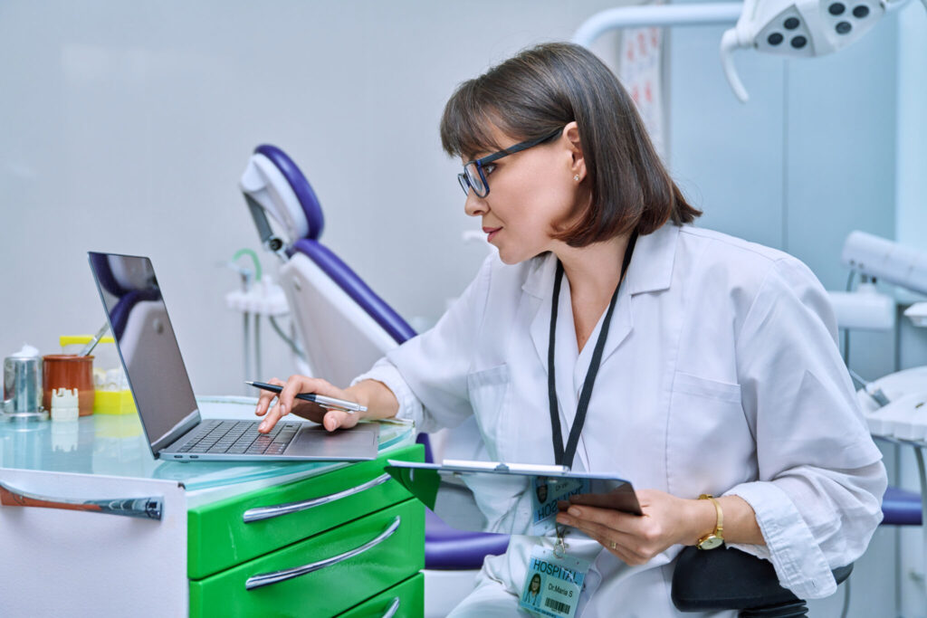 Doctor dentist working in office, using laptop, making notes on clipboard. Dentistry, medicine, hygiene, treatment, dental health care concept