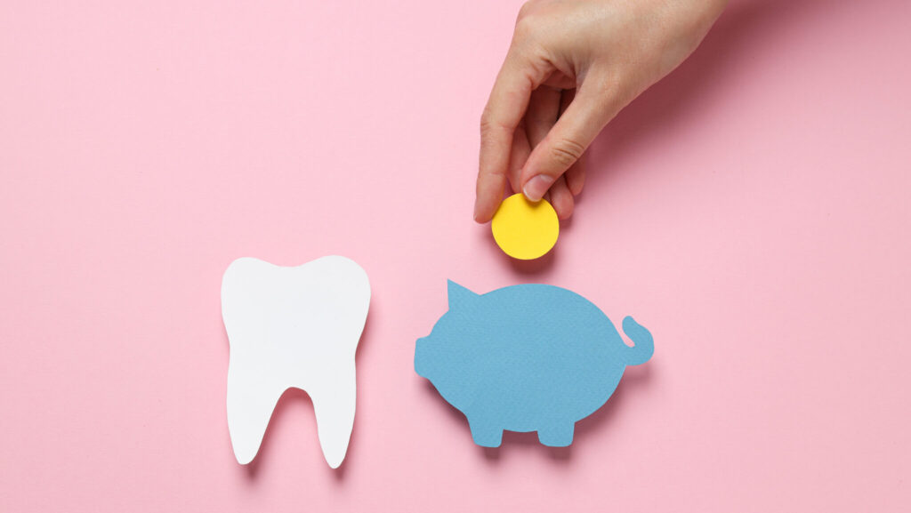 Paper tooth, piggy bank and coin in hand on pink background, top view
