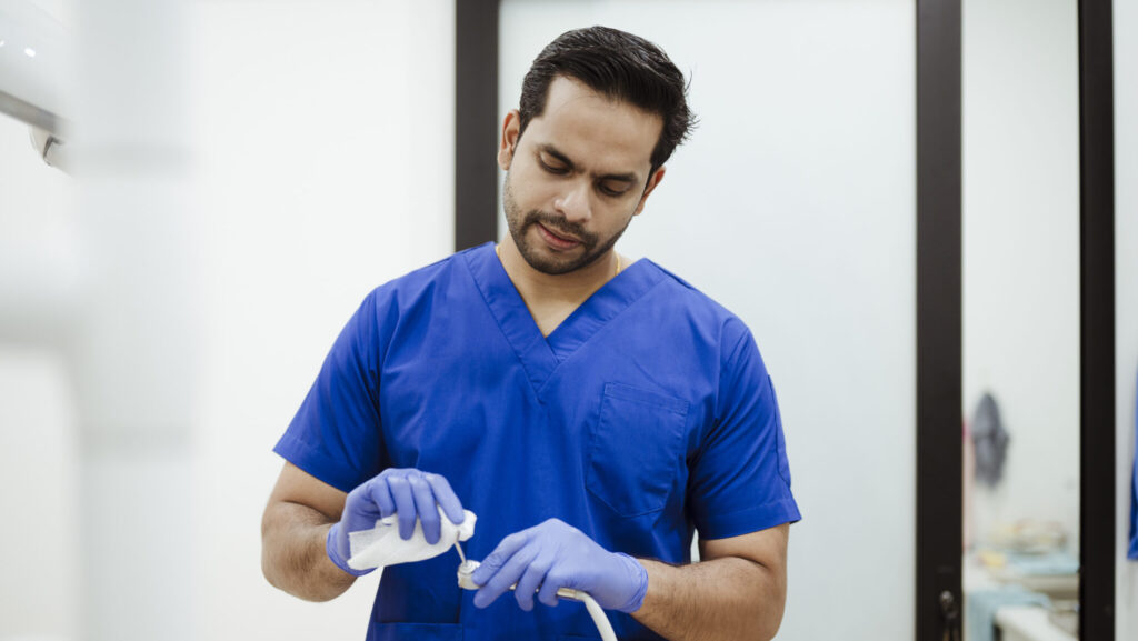 Dental professional maintaining hygiene by disinfecting tools and equipment in a bright clinic.