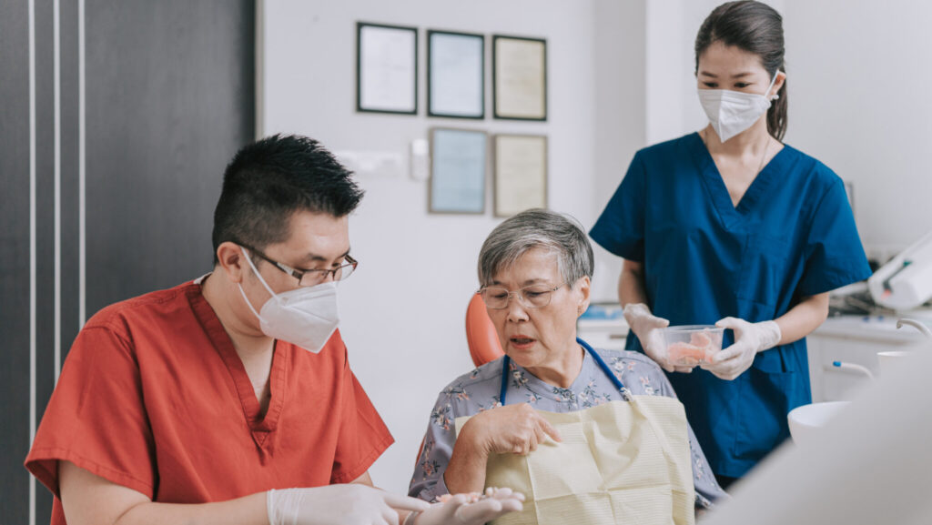 Asian Chinese male dentist explaining dental bridge on a tooth model to senior woman Patient