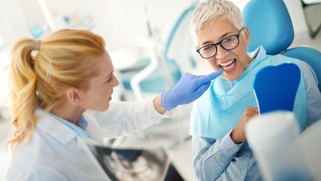 Closeup side view of an early 30's female dentist examining a senior female patient. She's showing her dental x-ray image and pointing at the exact tooth that's causing the pain.