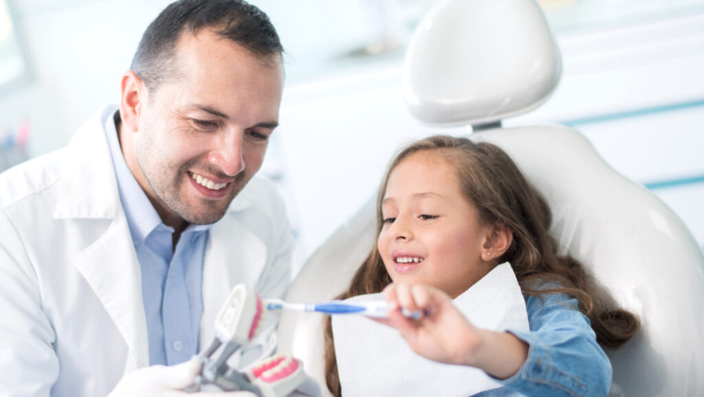 Beautiful girl at the dentist learning to brush her teeth properly and practicing on a denture