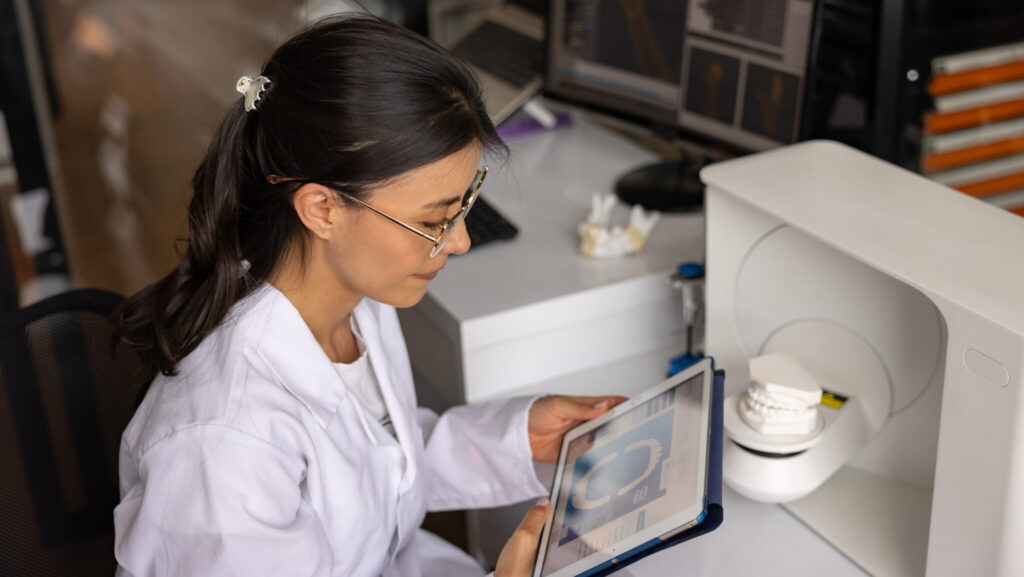 Latin American female engineer working at 3D printing lab and scanning a dental mold while using tablet - health technology concepts