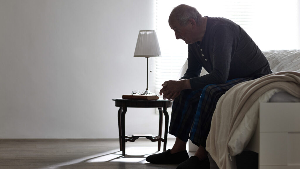 Elderly man sitting on bed looking serious - Indoors